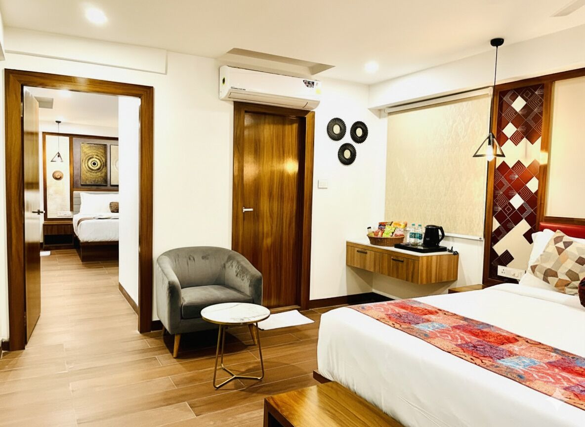 Une chambre d’hôtel avec un lit, un bureau et une chaise, une petite table et un canapé. Une porte donne accès à une autre pièce.