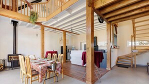 A spacious dining area with wooden chairs and a table set for two, a kitchen in the background, and a staircase leading to an upper level. - Family Cottage in the Countryside (Noyant-Villages)