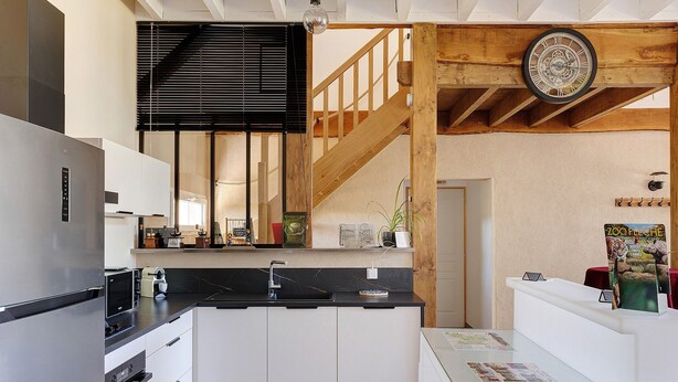 A modern kitchen with a black countertop, white cabinets, a stainless steel refrigerator, and a wooden staircase. - Family Cottage in the Countryside (Noyant-Villages)