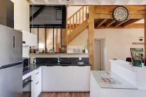 A modern kitchen with a black countertop, white cabinets, a stainless steel refrigerator, and a wooden staircase.