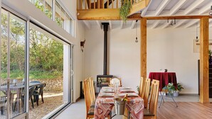 A dining area with a table set for four, a wood-burning stove, and a view through large glass doors. - Family Cottage in the Countryside (Noyant-Villages)