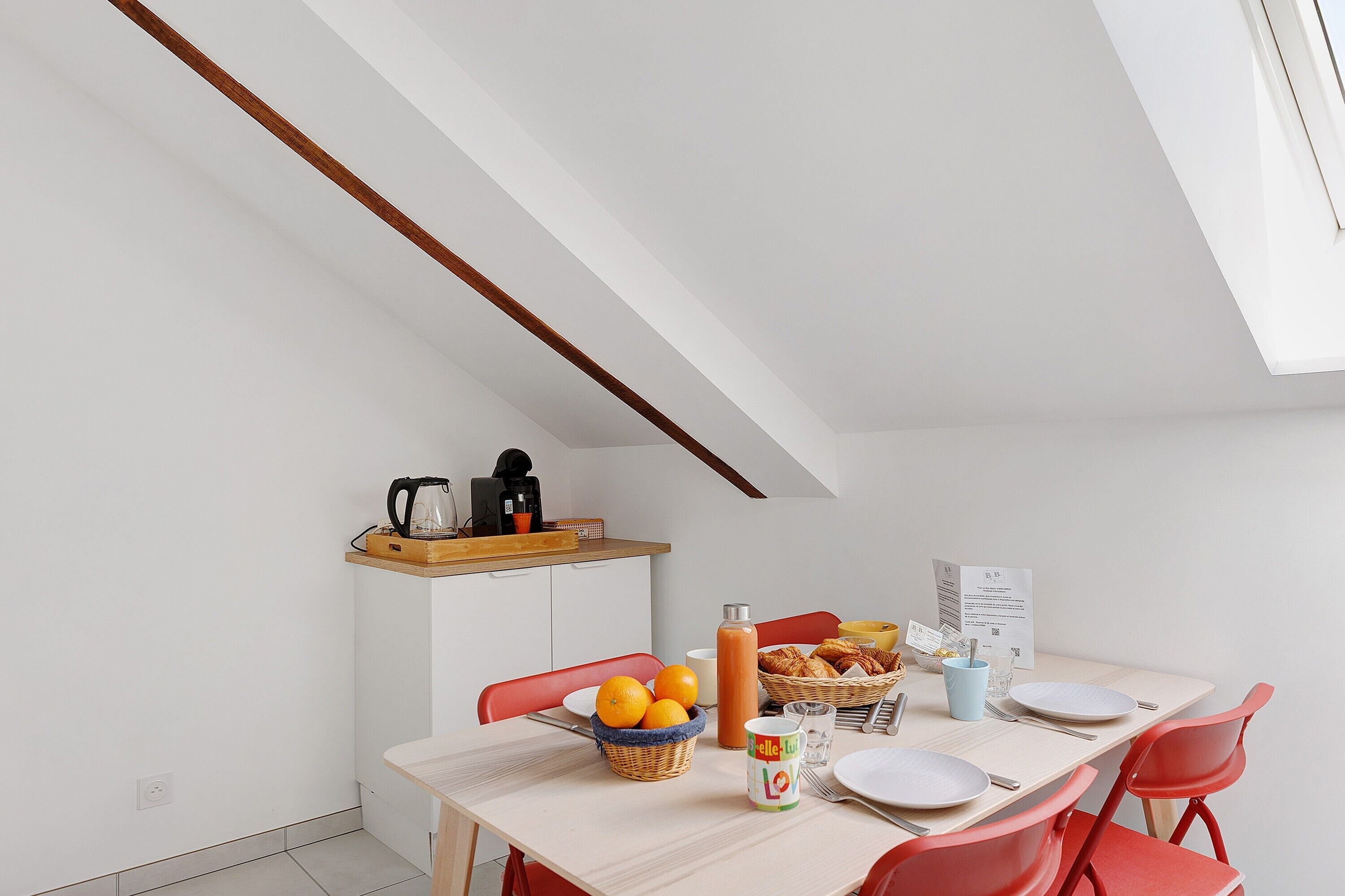 Une cuisine moderne équipée d’un coin petit-déjeuner comprenant un panier d’oranges, une bouteille de jus et une machine à café.