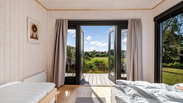 Ein Schlafzimmer mit zwei Betten, Holzboden, einem großen Fenster und Blick auf eine grüne Landschaft.