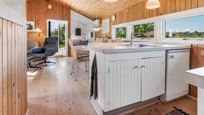 Eine moderne Küche mit Holzvertäfelung, einer zentralen Kochinsel mit Spüle, Pendelleuchten und Blick durch große Fenster.