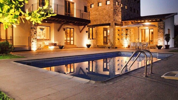 A two-story house with a swimming pool, outdoor seating, and a stone facade.