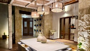 A dining area with a large table, striped cushioned chairs, hanging wicker chandeliers, and stone walls. - Villa Grand Zeus - A place to slow down (Anogyra)