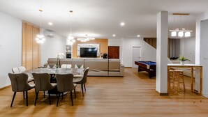 Un saló modern amb zona de menjador, billar i cuina al fons.