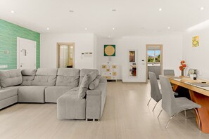 A modern living room with a sectional sofa, a dining area with a glass table, and a kitchen visible through an open door. - Country House in a Top Location with Mountain Views, Wi-Fi and Air Conditioning (Coin)