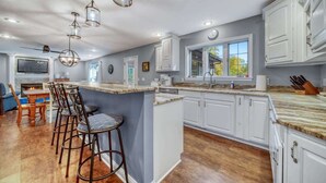 A spacious kitchen with white cabinets, a large island with bar stools, pendant lighting, and a view of the outdoors.
