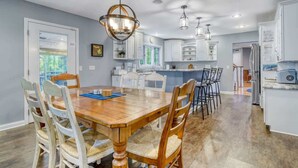 A spacious kitchen with white cabinets, a wooden dining table with chairs, and pendant lighting.