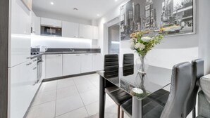 Una cocina moderna con armarios blancos, encimera negra y una zona de comedor con mesa de vidrio y sillas negras.