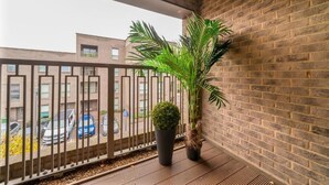 Un balcón con una planta en maceta, un muro de ladrillo y vistas a coches estacionados y edificios.