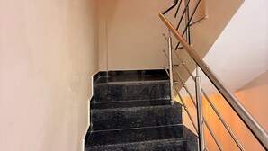 A staircase with black marble steps and a metal handrail, leading to a room with a light-colored wall and a wall-mounted light fixture. - Hotel Roshan (Ujjain)