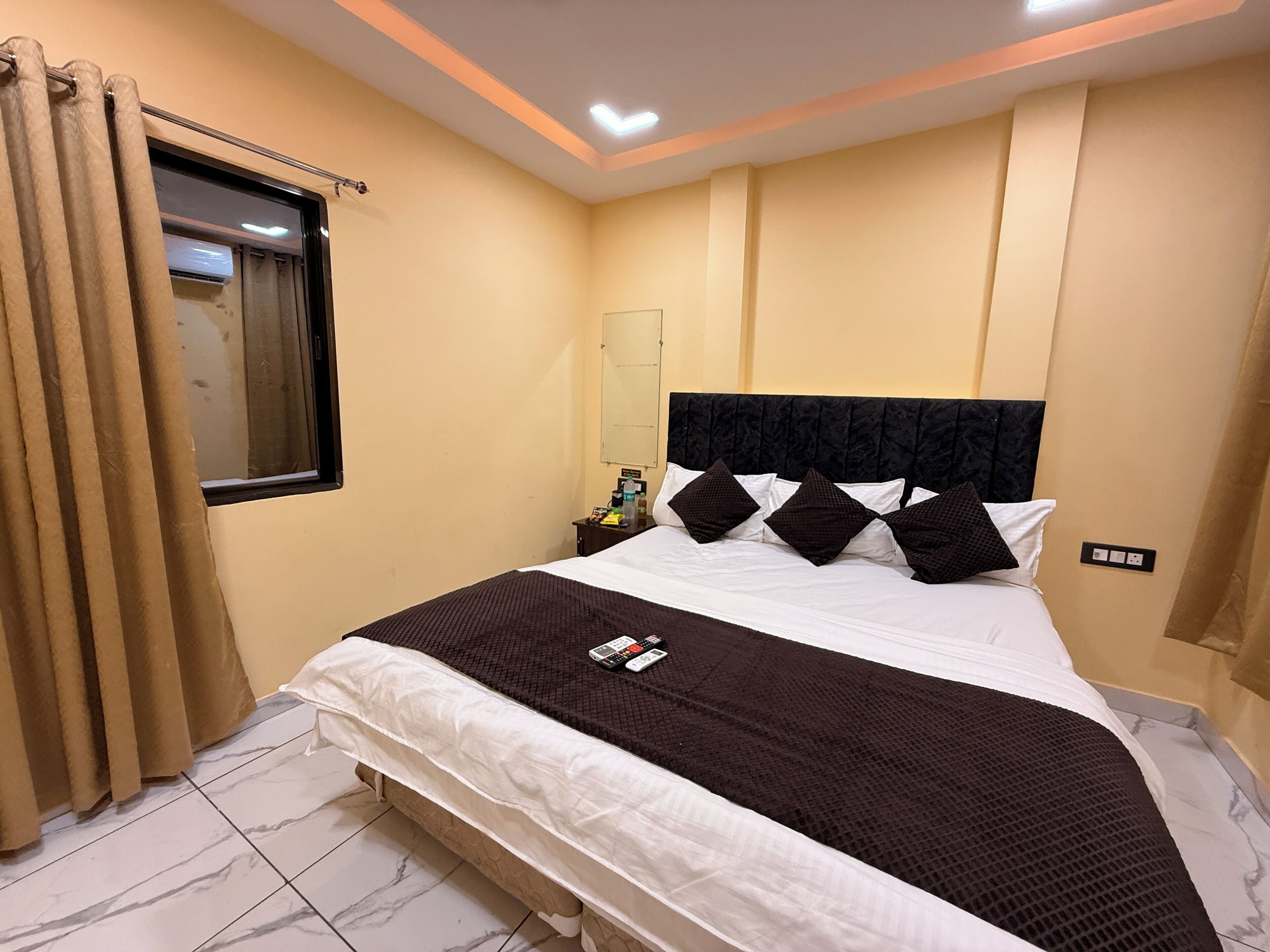 Quarto de hotel com cama, cortinas, mesa de cabeceira e espelho.
