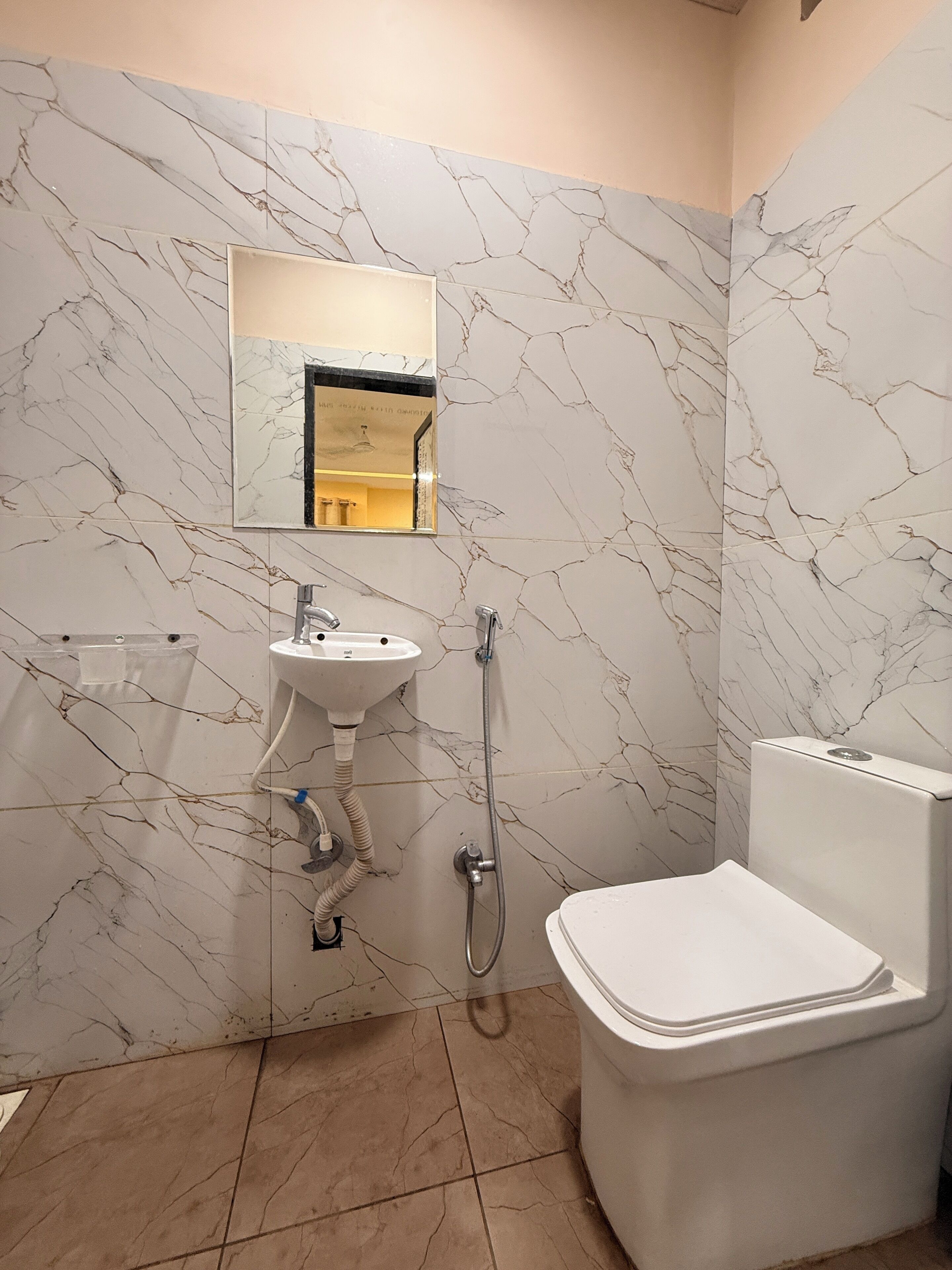A bathroom with a marble-patterned wall, a sink, a toilet, and a shower.