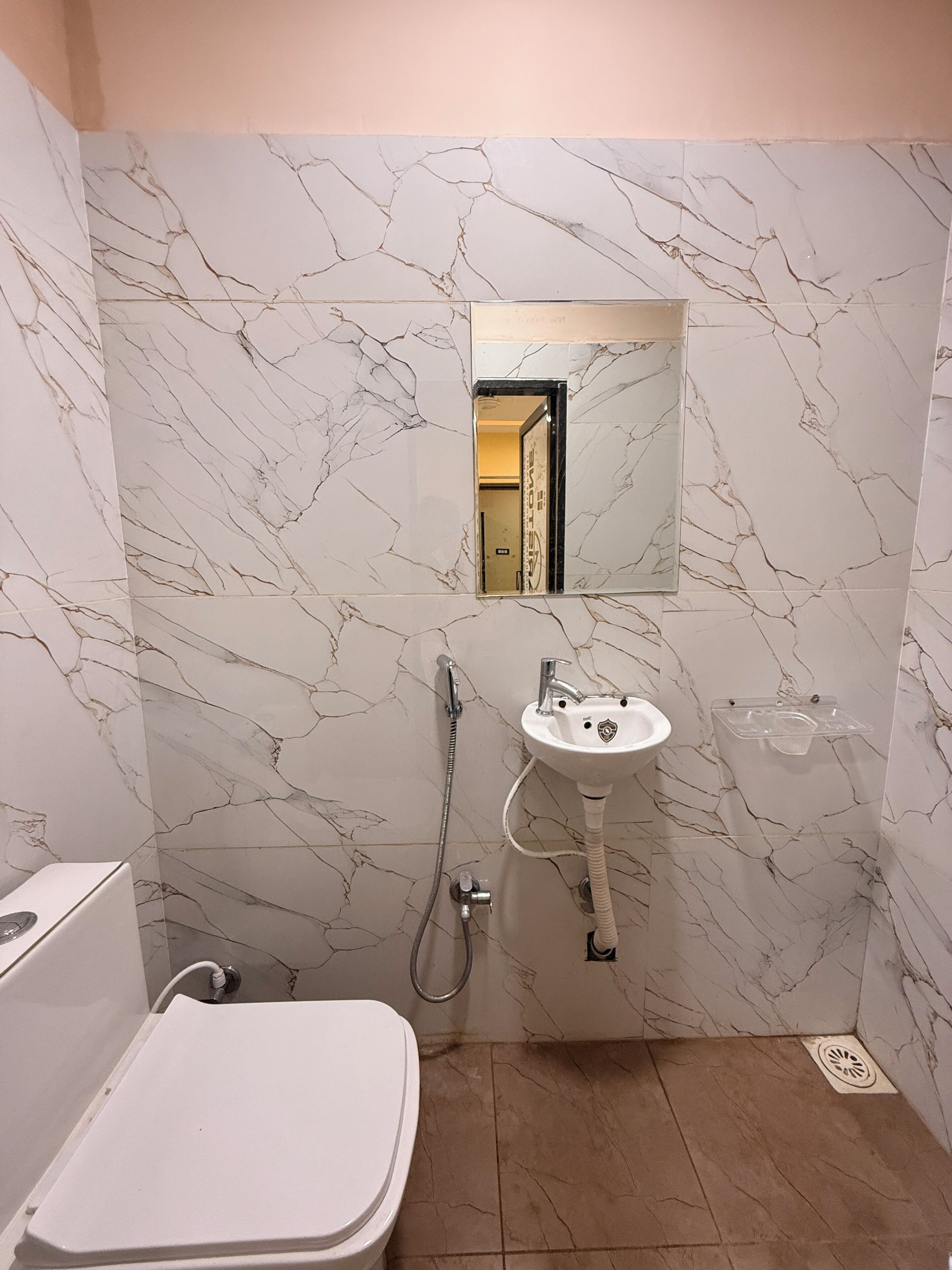 Un baño con pared de mármol blanco, un lavamanos, un espejo y una ducha.