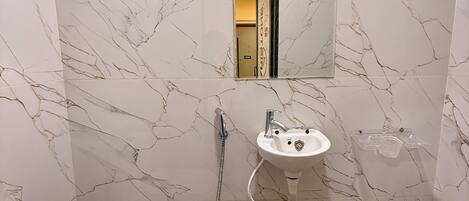 Un baño con pared de mármol blanco, un lavamanos, un espejo y una ducha.