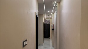 A hallway with a marble floor, beige walls, and a ceiling with recessed lighting. - Hotel Roshan (Ujjain)