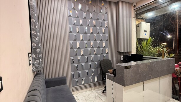 A reception area with a grey sofa, a patterned wall, a reception desk, and a plant. - Hotel Roshan (Ujjain)