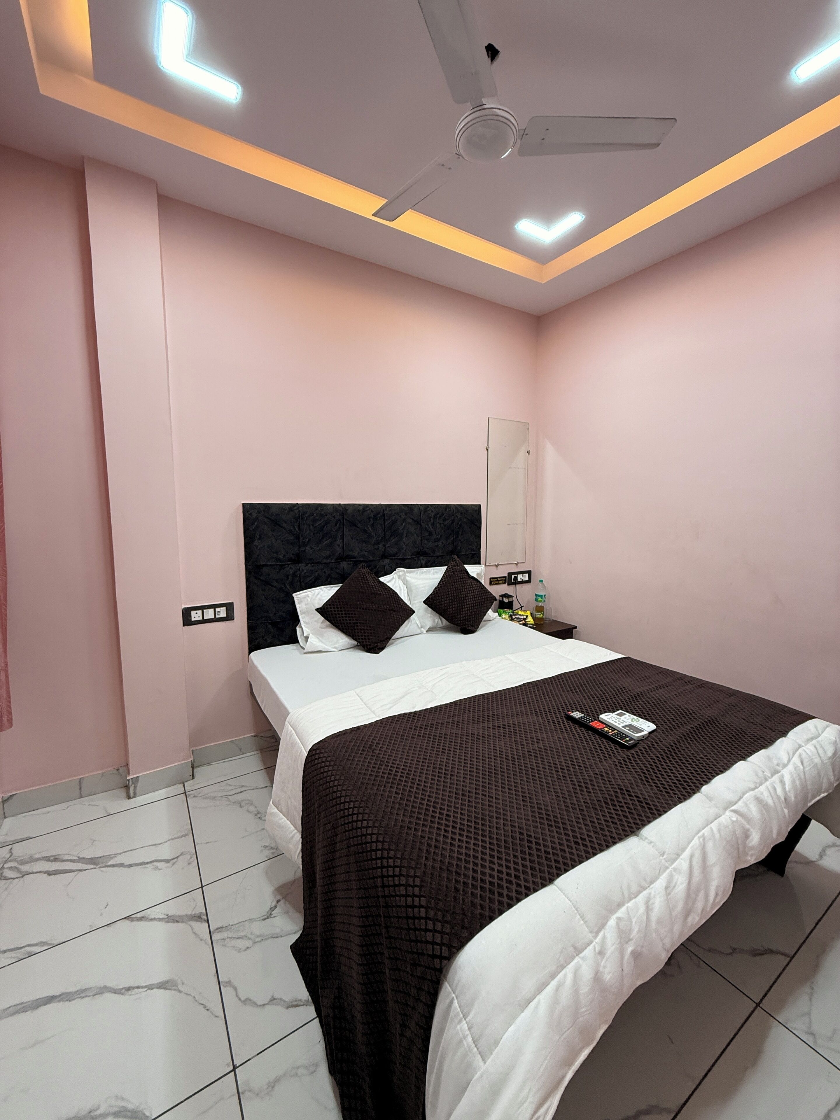 A bedroom with a bed, a ceiling fan, and a nightstand with a bottle and remote control.