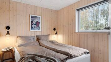 A bedroom with a bed, two bedside lamps, a window, and a framed picture on the wall.