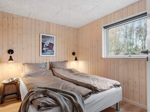 A bedroom with a bed, two bedside lamps, a window, and a framed picture on the wall.