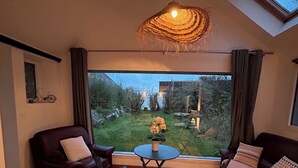 A cozy living room with a large window, a dark brown sofa, a small round table, and two blue chairs.