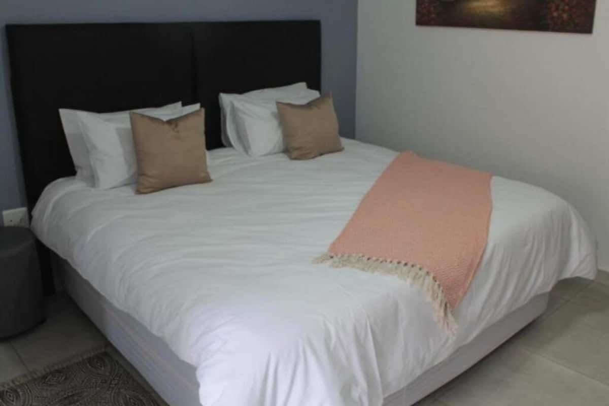 Una cama bien hecha con sábanas blancas y una manta rosa, un cabecero oscuro y un cuadro en la pared.