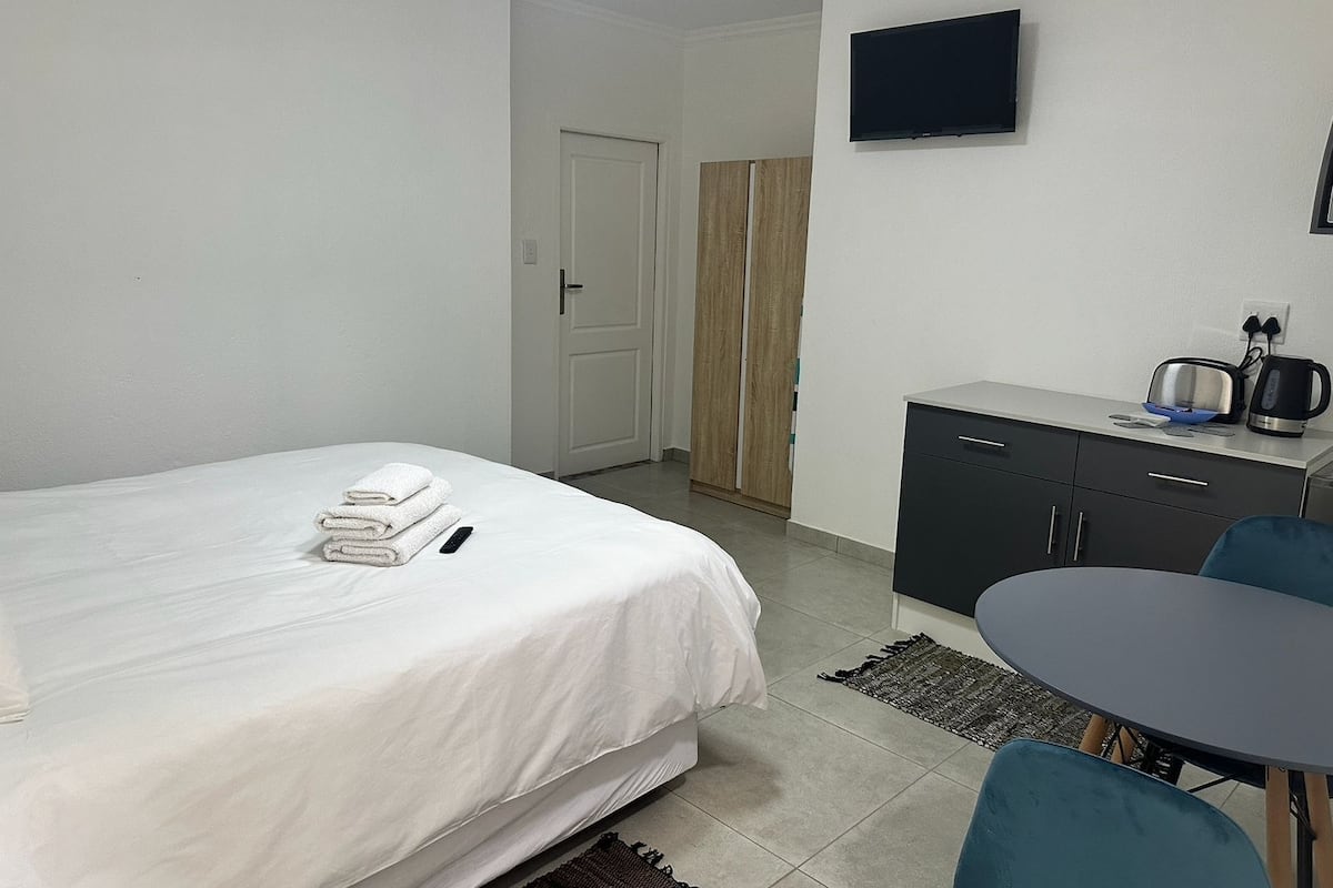 Una habitación de hotel con cama, escritorio, silla, televisor y kitchenette.