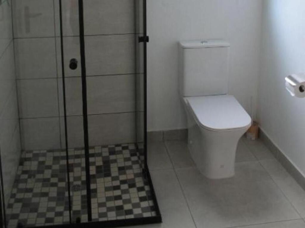 Un baño con suelo de baldosas, inodoro y zona de ducha con mampara de cristal.