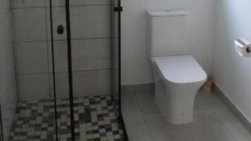 Un baño con suelo de baldosas, inodoro y zona de ducha con mampara de cristal.