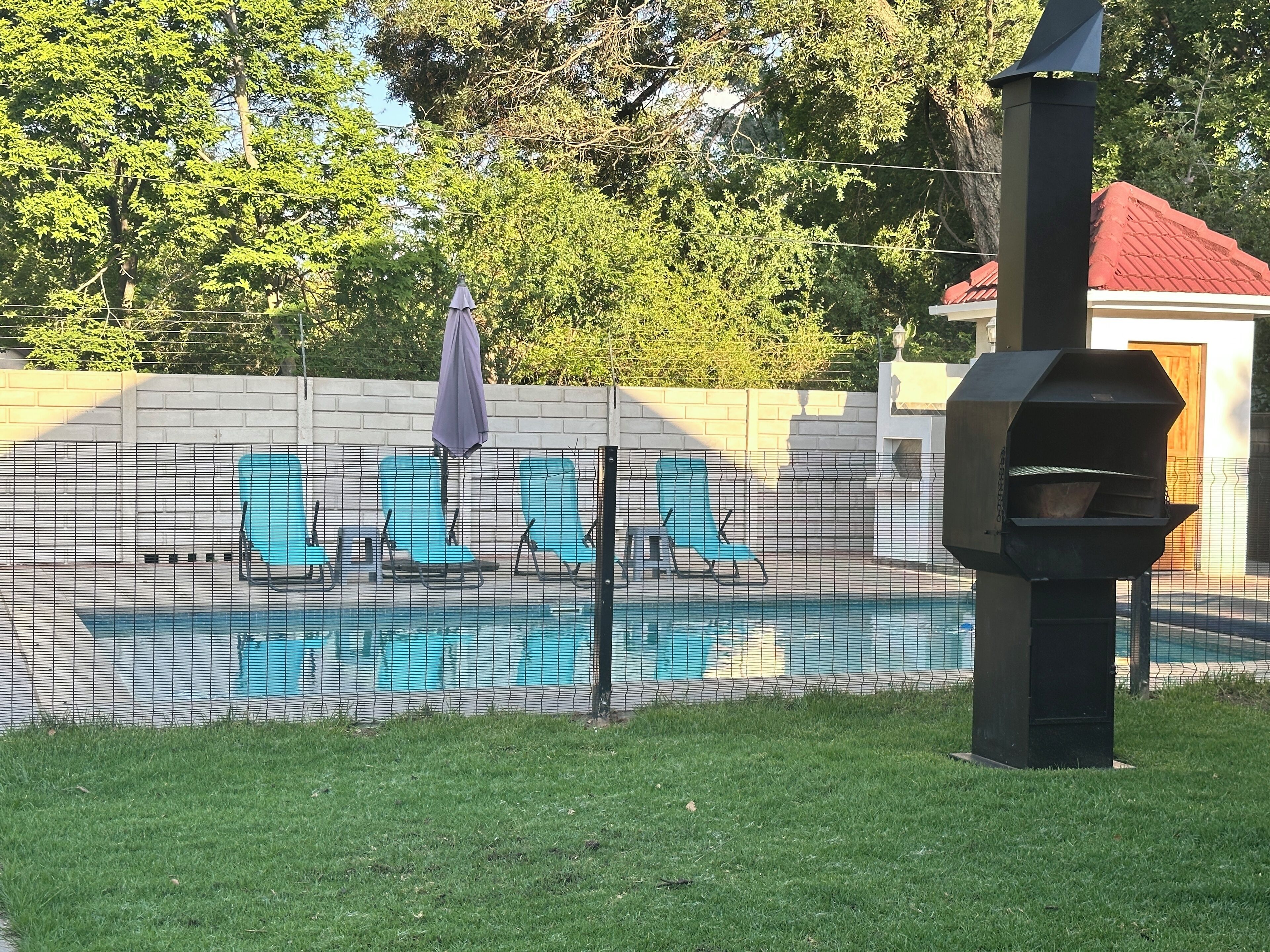 A backyard with a swimming pool, lounge chairs, a barbecue grill, and a fenced area.