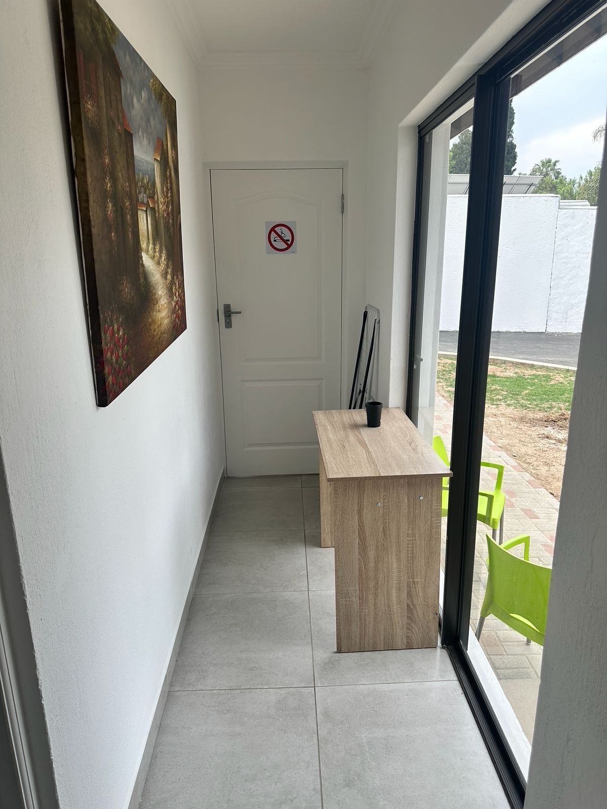 Een gang met een houten bureau, een deur met een rookverbodsgebaar en een uitzicht buiten door een glazen deur.