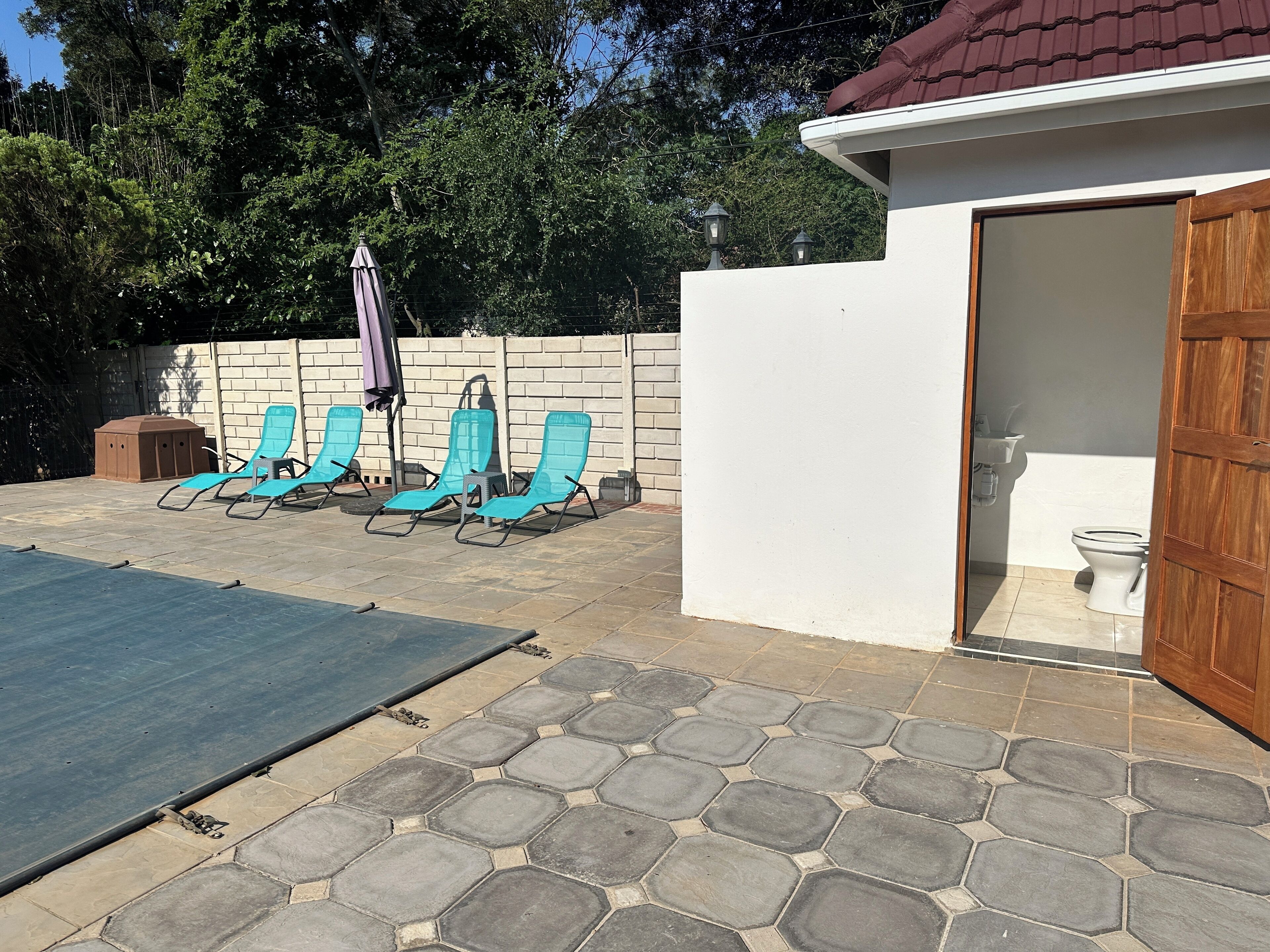 A patio with four blue lounge chairs, a barbecue grill, and a covered area with an umbrella.
