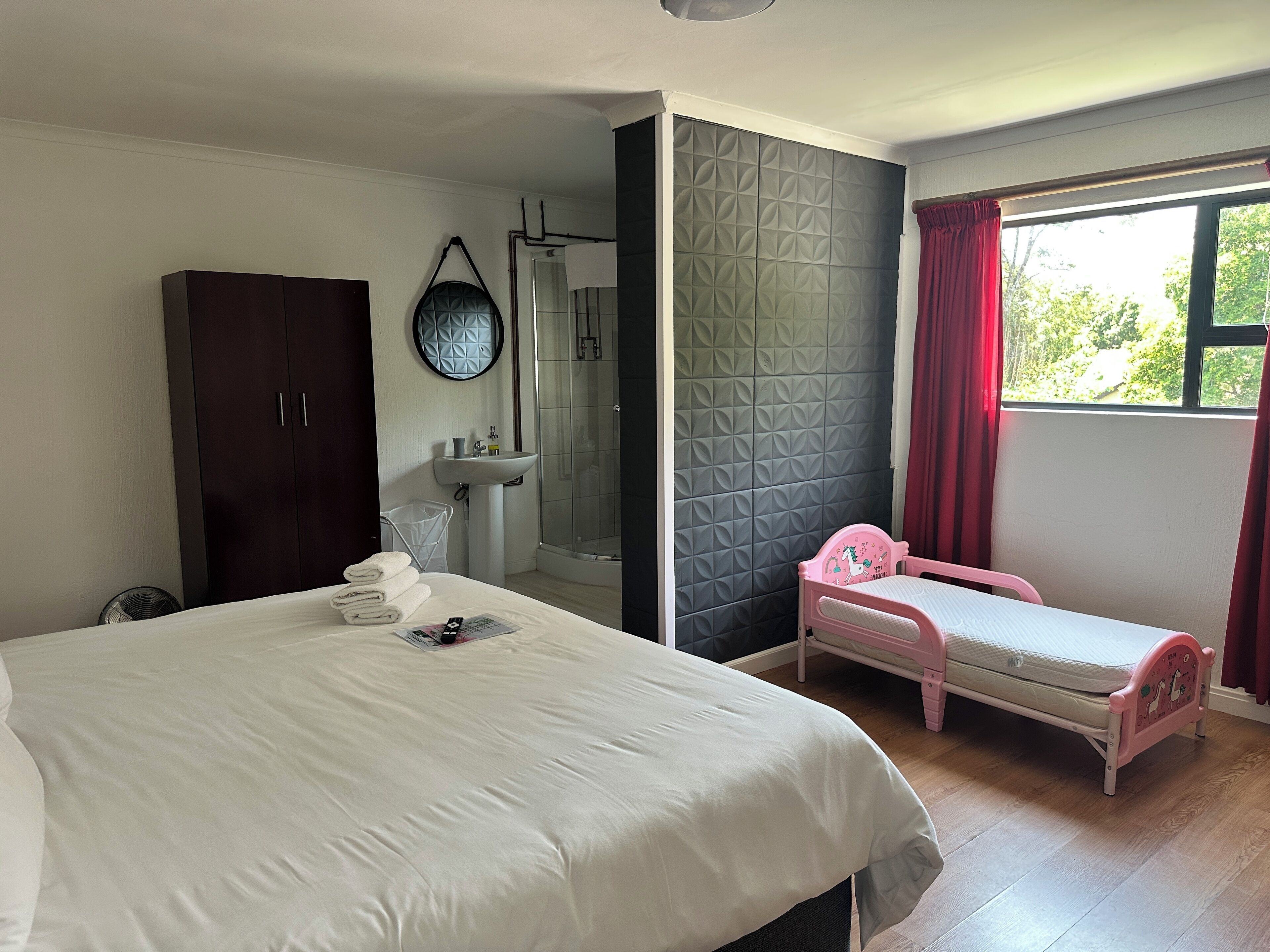 A bedroom with a large bed, a smaller bed, a wardrobe, a sink, and a shower.