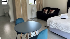 A hotel room with a bed, a desk, a chair, a table, a window, and a door.