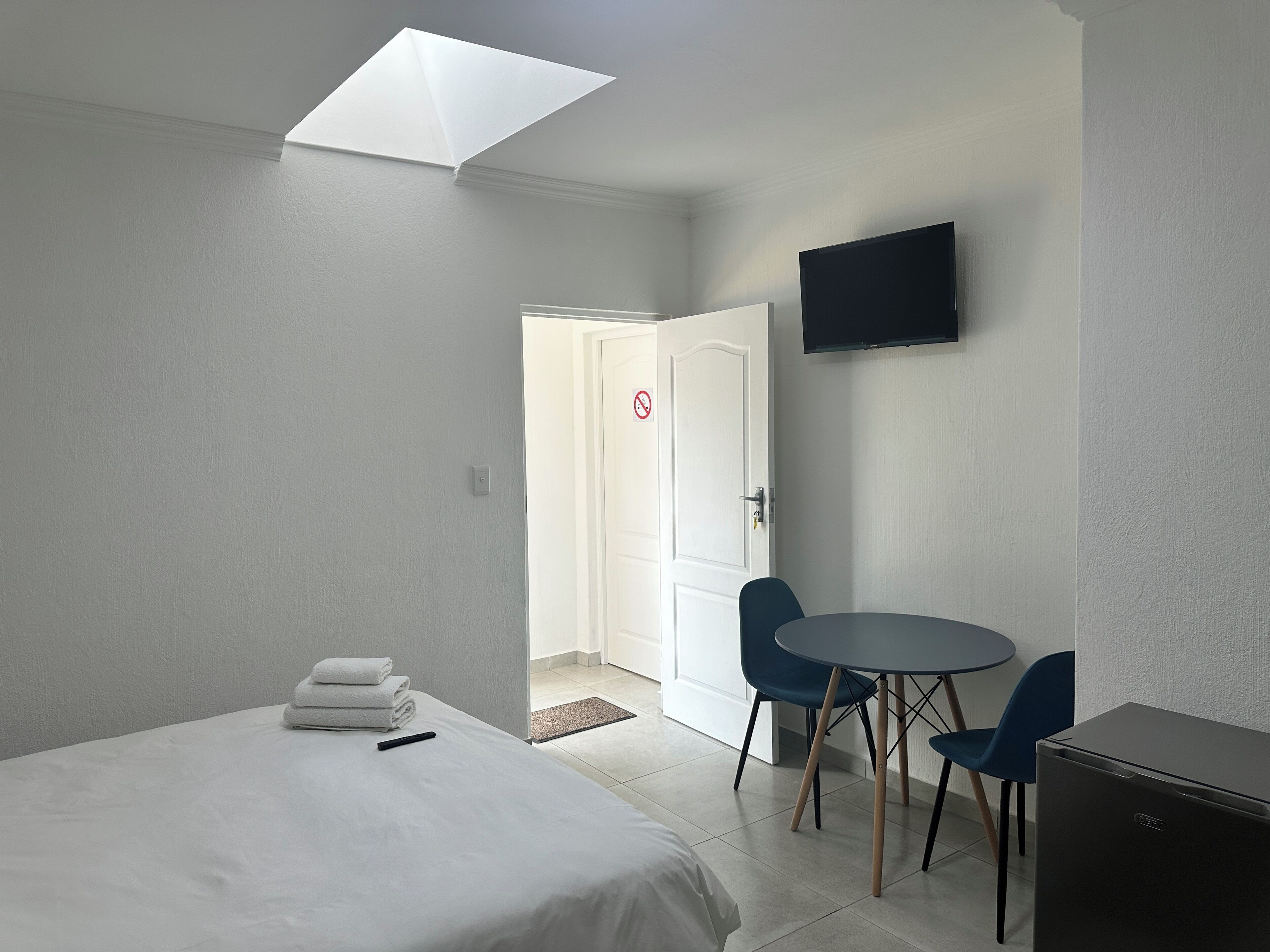 A hotel room with a bed, a desk with chairs, a flat-screen TV, and a door with a no-smoking sign.