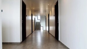 A long, narrow hallway with a tiled floor and doors on both sides leading to rooms. - Aatithya Residency (Rajgurunagar)