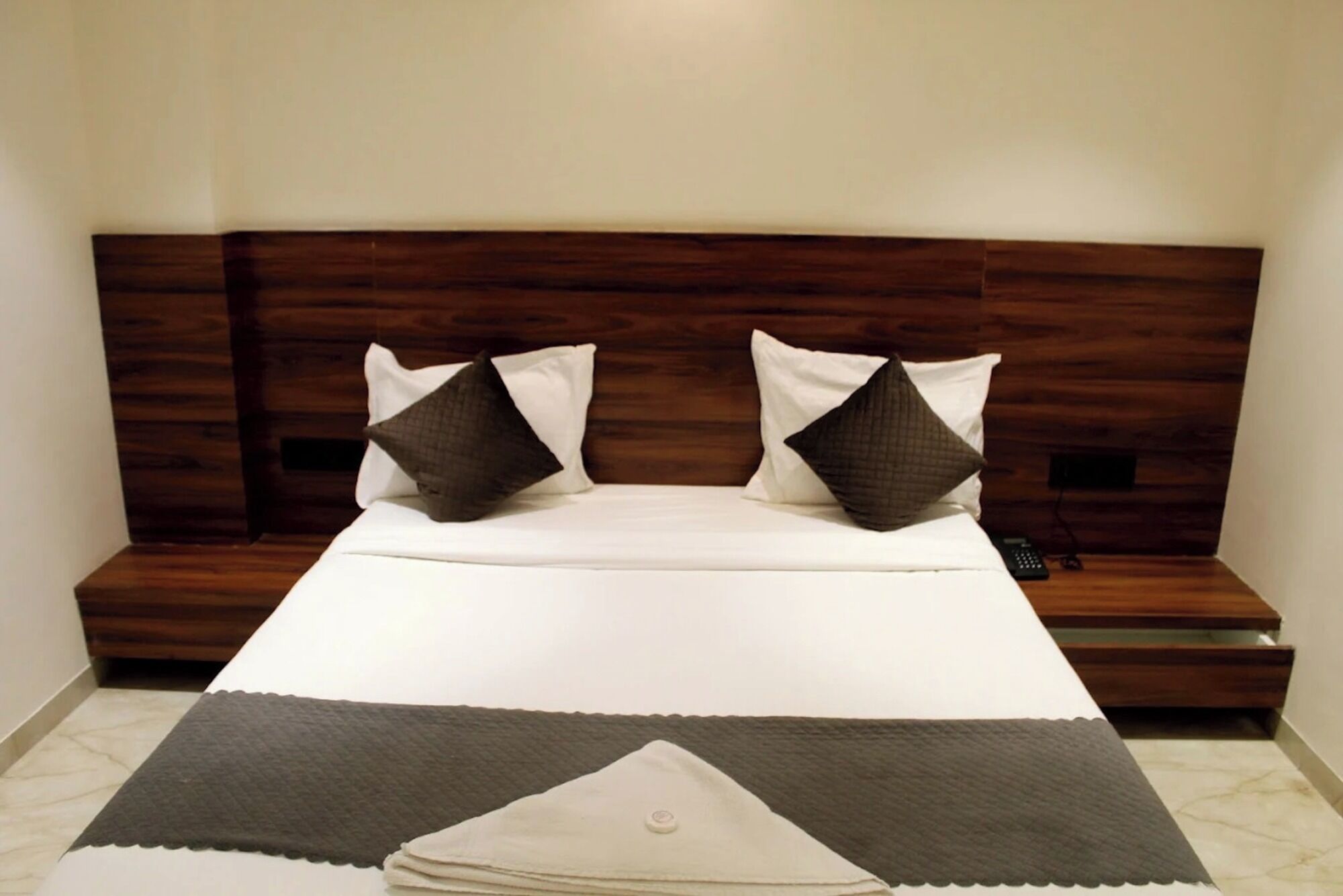 A neatly made bed with a wooden headboard, two pillows, and a bedside table with a remote control.
