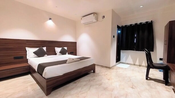 A modern bedroom with a wooden headboard, a large bed with white bedding, a small bedside table, and a chair. - Aatithya Residency (Rajgurunagar)