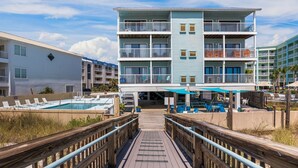 Un hôtel à plusieurs étages doté d’une piscine, d’un espace extérieur aménagé avec des sièges et d’une promenade en bois menant à l’entrée.