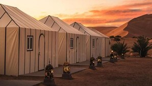 A row of tents with arched doorways, set against a desert landscape at sunset. - Merzouga VIP Luxury Camp (Merzouga)