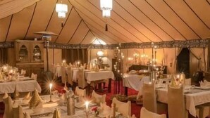 A tented dining area with tables set for a meal, chandeliers, and a red carpet. - Merzouga VIP Luxury Camp (Merzouga)
