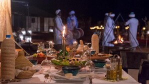 A table set for a meal with various dishes and drinks, candles, and a fire pit in the background. - Merzouga VIP Luxury Camp (Merzouga)