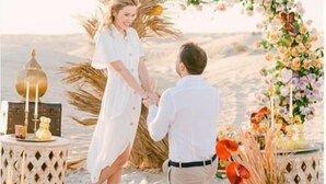 A beach setting with a couple holding hands under a floral arch, surrounded by decorative items and a lantern. - Merzouga VIP Luxury Camp (Merzouga)