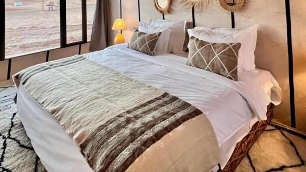 A tent-style room with a bed, a lamp, and wall decorations including hats and mirrors. - Merzouga VIP Luxury Camp (Merzouga)