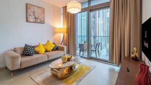 A modern living room with a sofa, a coffee table, a TV, and a balcony with a city view. - Luxury 1BR in Marina Gate with Infinity Pool (Dubai)