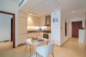 A modern kitchen with white cabinets, a dining table with chairs, and a small refrigerator.