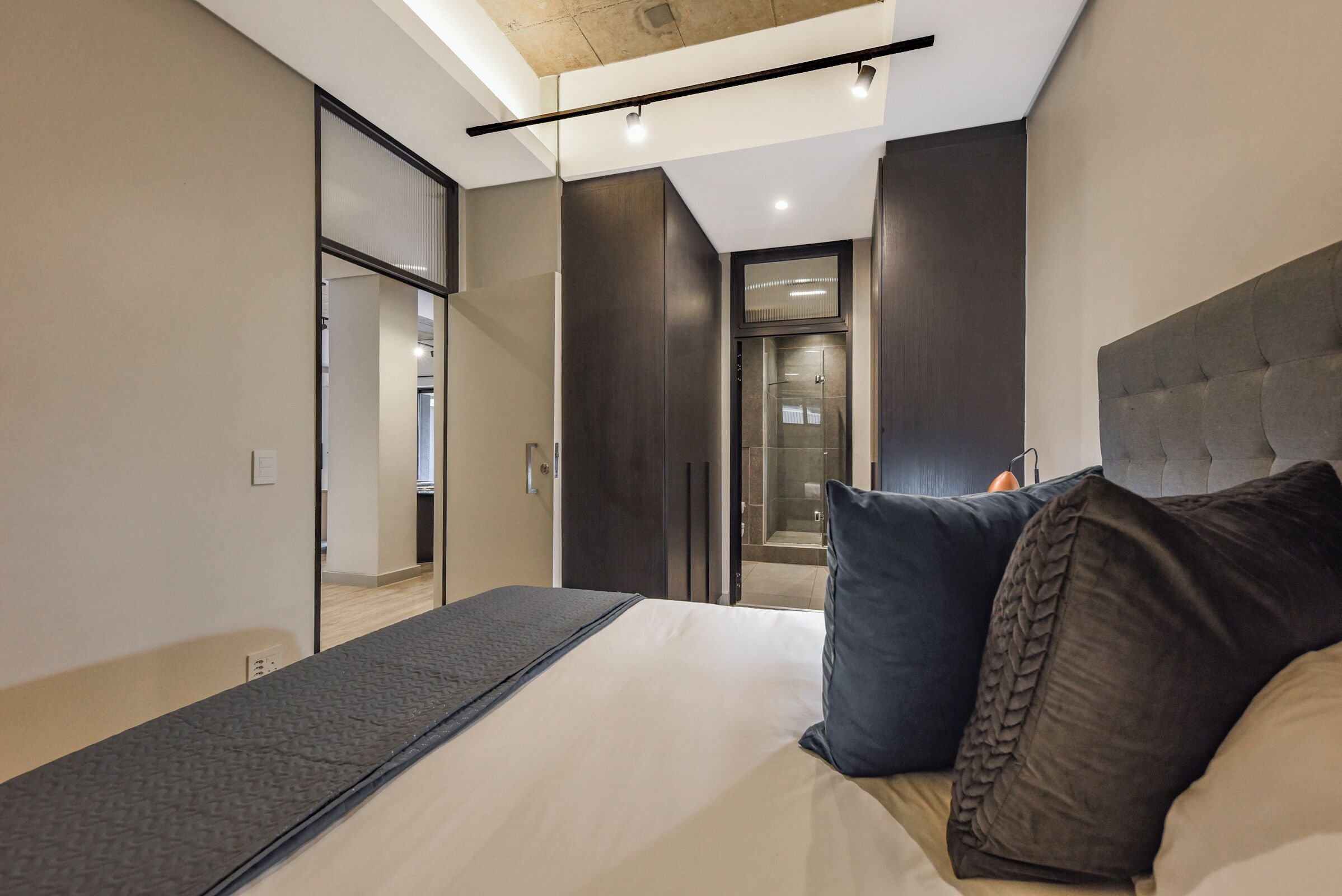A modern bedroom with a bed, dark headboard, and a walk-in closet.