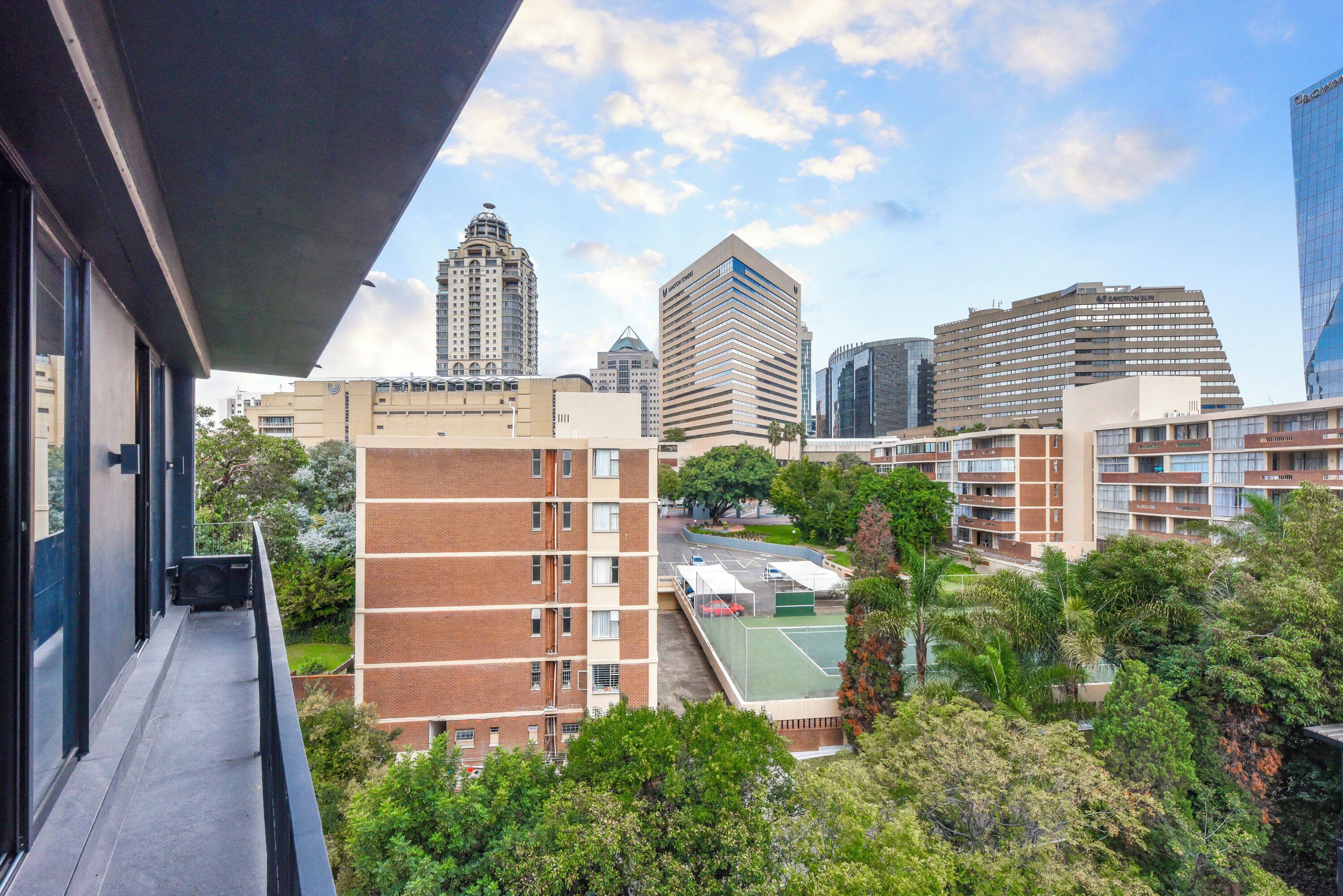 A high-rise building with a modern design, surrounded by greenery and other buildings.